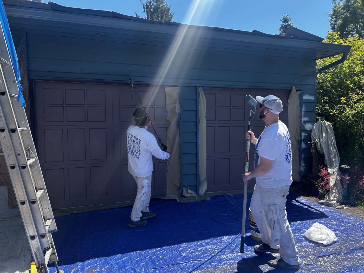 Two painters with rollers painting garage doors over drop cloths